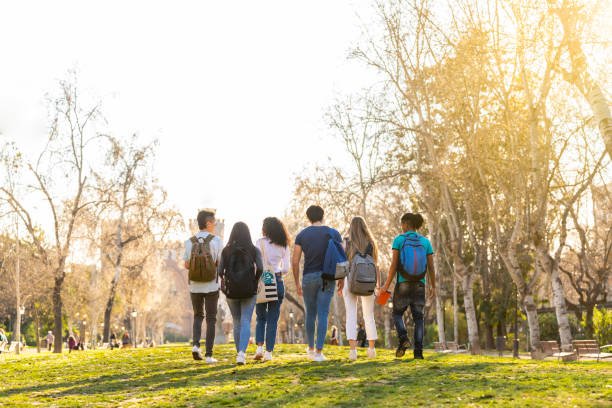 a row of young multi ethnic students walking together in the park. back view